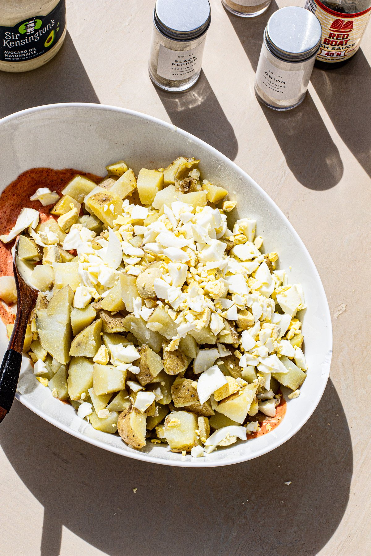 Palabok potato salad ingredients being mixed into a bowl.