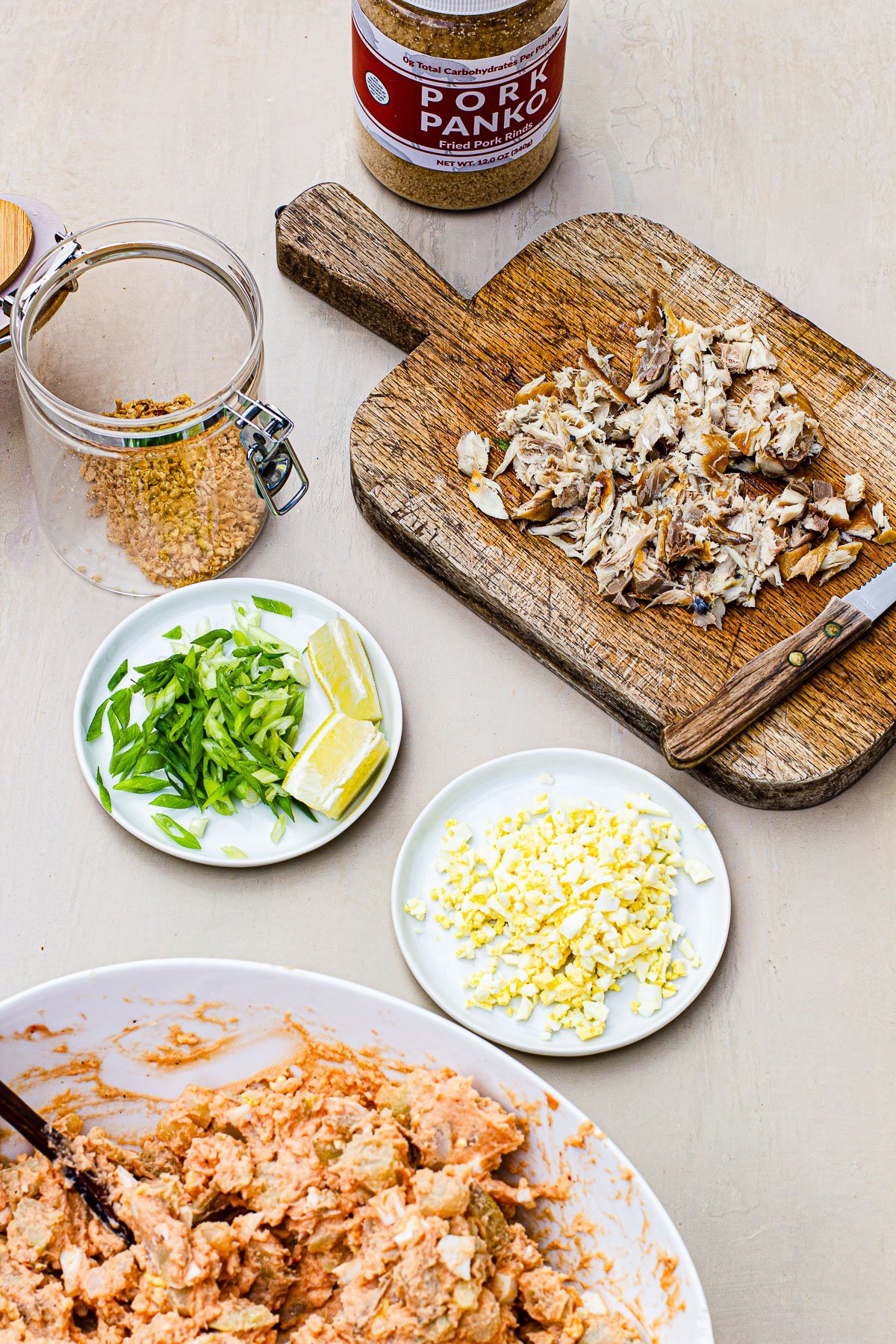 Dried fish flakes on a wooden board, pork panko in a jar.  Sliced green onions on a plate with lemon wedges.  Fried garlic in a glass jar.