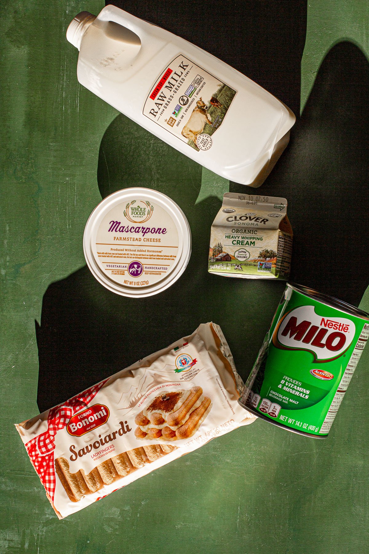 Pint of Milk, container of marsapone, container of cream, packet of savoiardi, can of milo on a green backdrop.