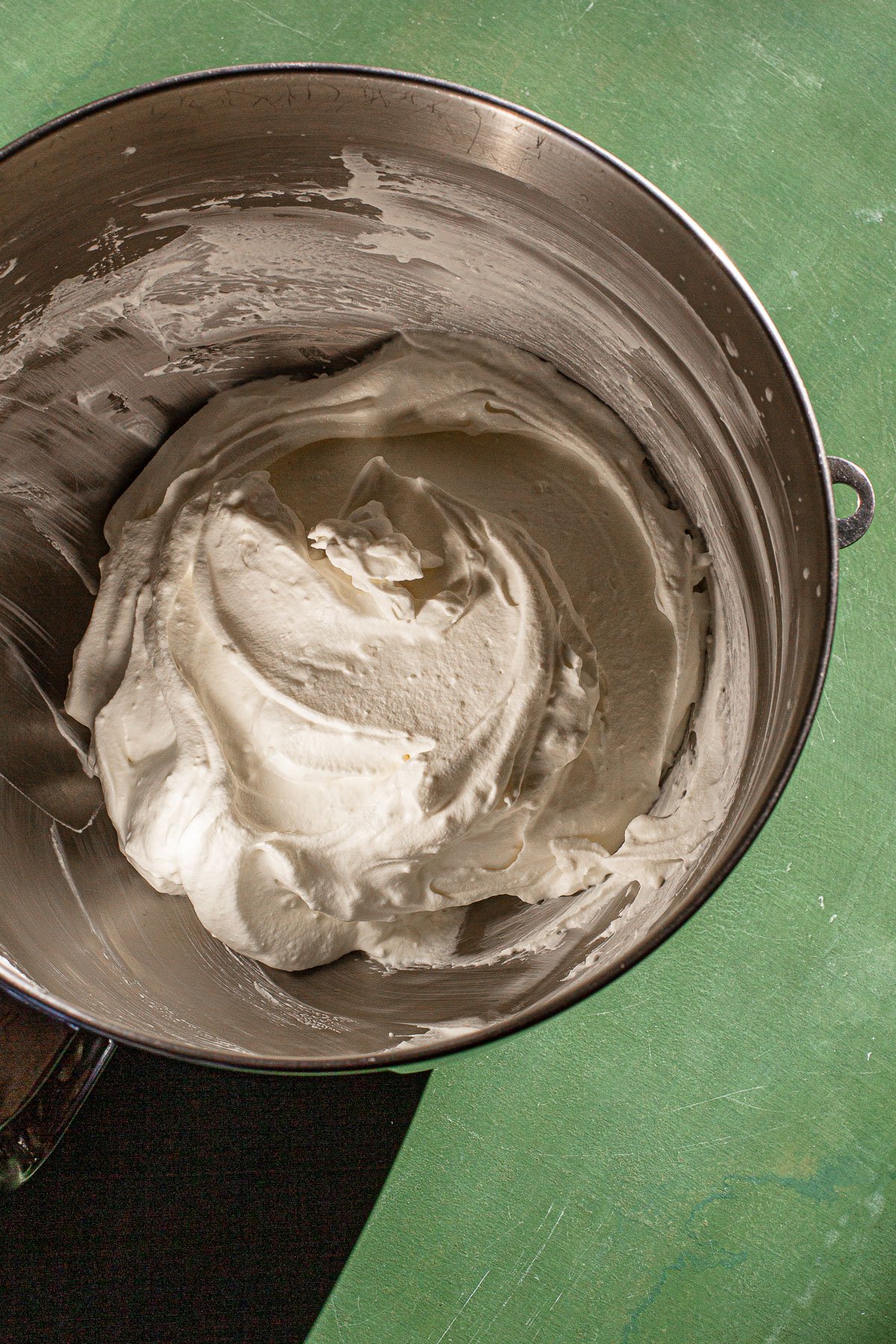 Whipped cream and marscapone in a mixing bowl on a green backdrop.