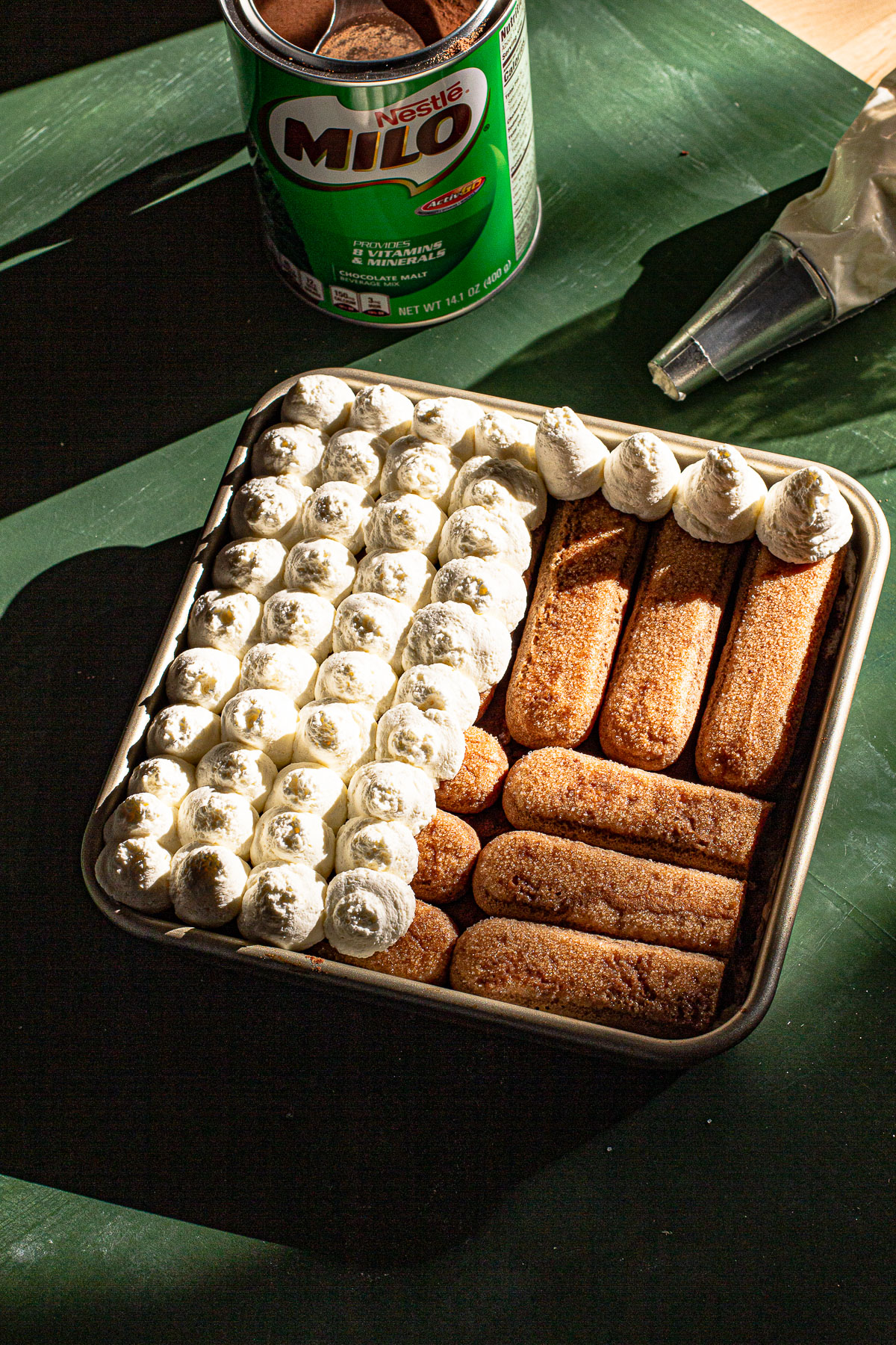 Piped dots of whipped cream on top of milo soaked lady fingers.