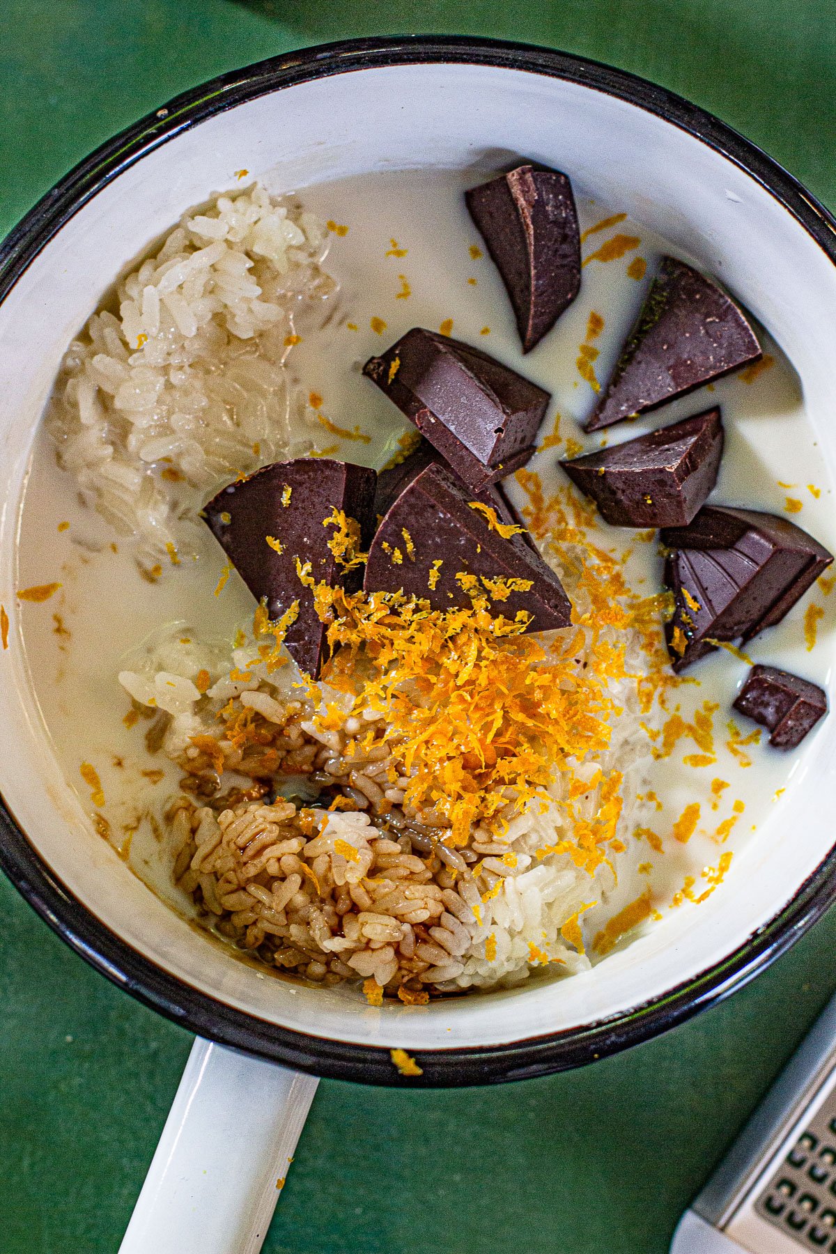 Mixture of sticky rice, coconut milk, date syrup, chocolate chunks and orange zest in a sauce pan.