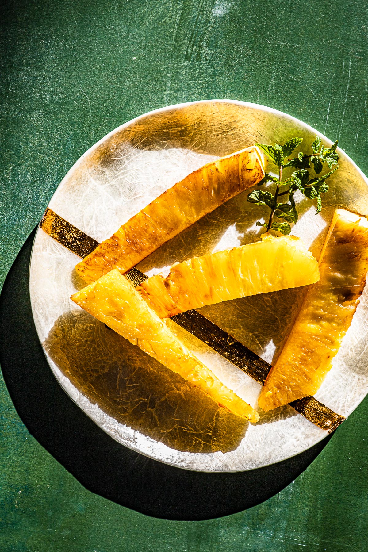 Grilled pineapple and fresh mint on a capiz and gold plate.  On a green backdrop.