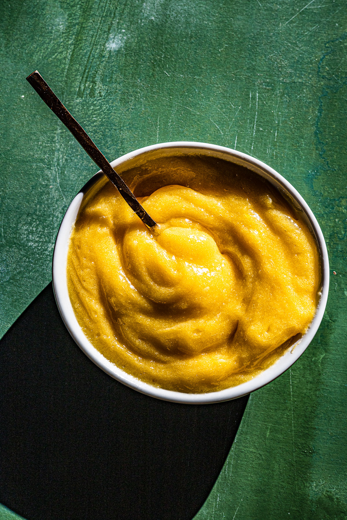Calamansi Curd in a bowl with a gold spoon.  On a green backdrop.