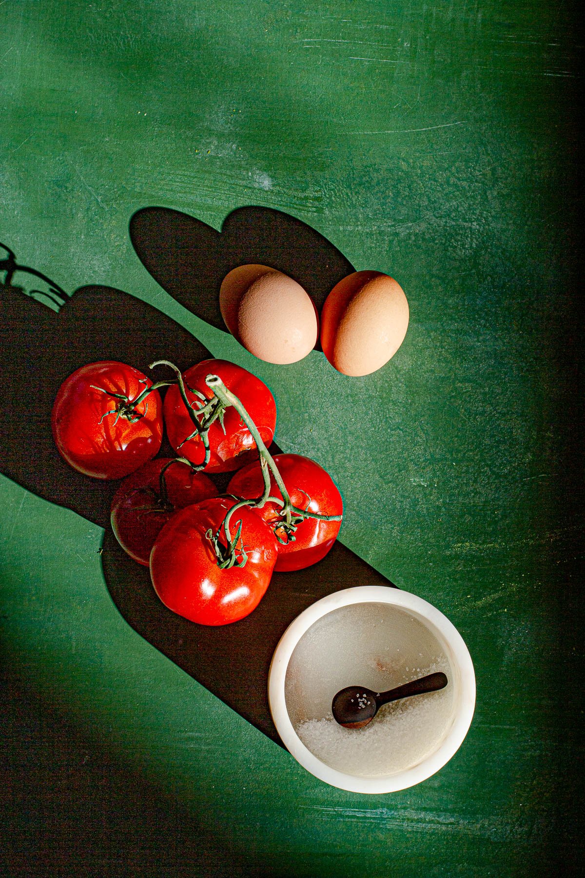 2 Eggs, 5 Tomatoes on the vine, some salt in a marble container with a small wooden spoon.