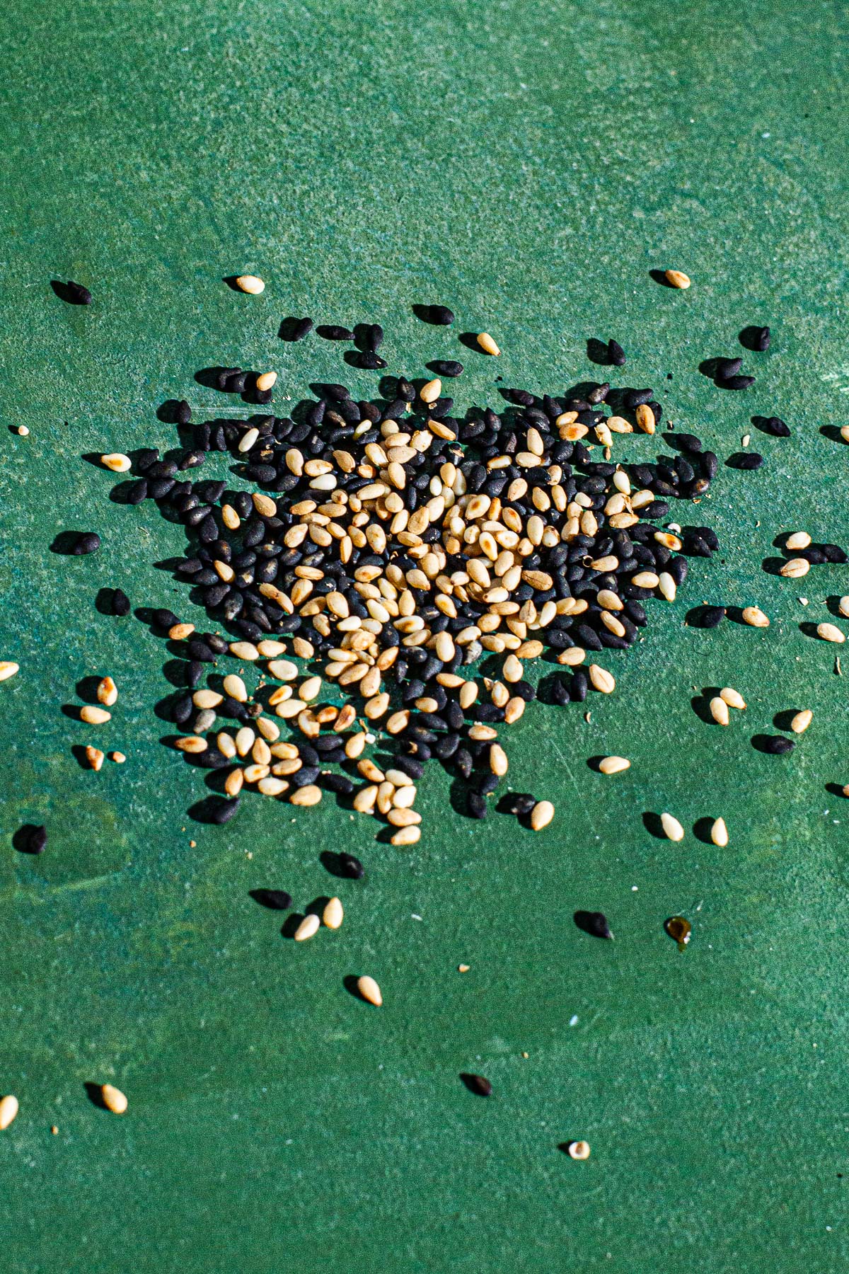 Mix of white and dark sesame seeds on a green backdrop.