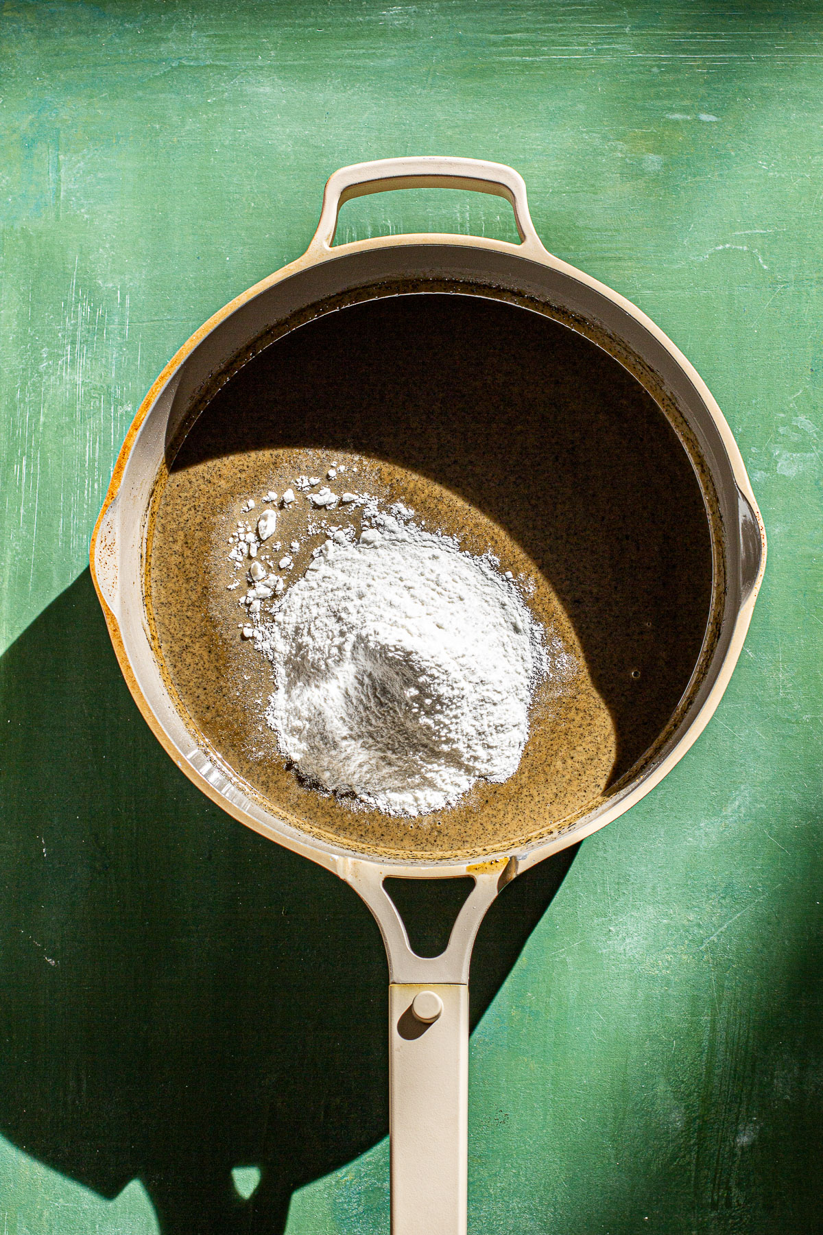 Coconut milk mixture with glutinous rice flour in a pan on a green backdrop.