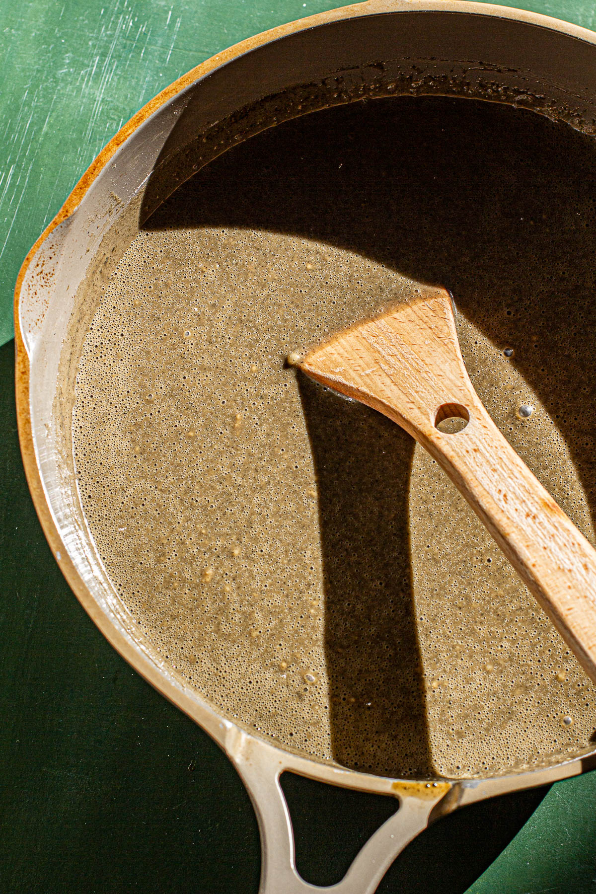 Kalamay mixture in a pan with a wooden spoon in a non stick pan on a green backdrop.