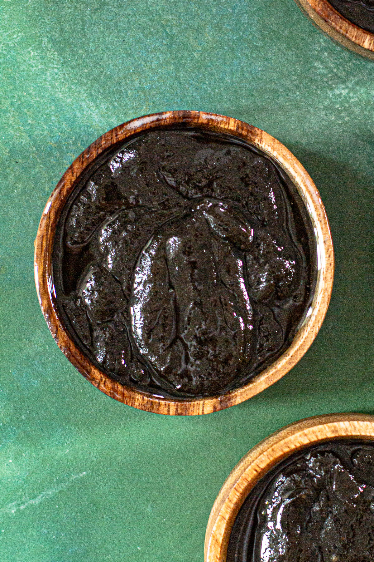 Black sesame kalamay in a wooden bowl on a green backdrop.