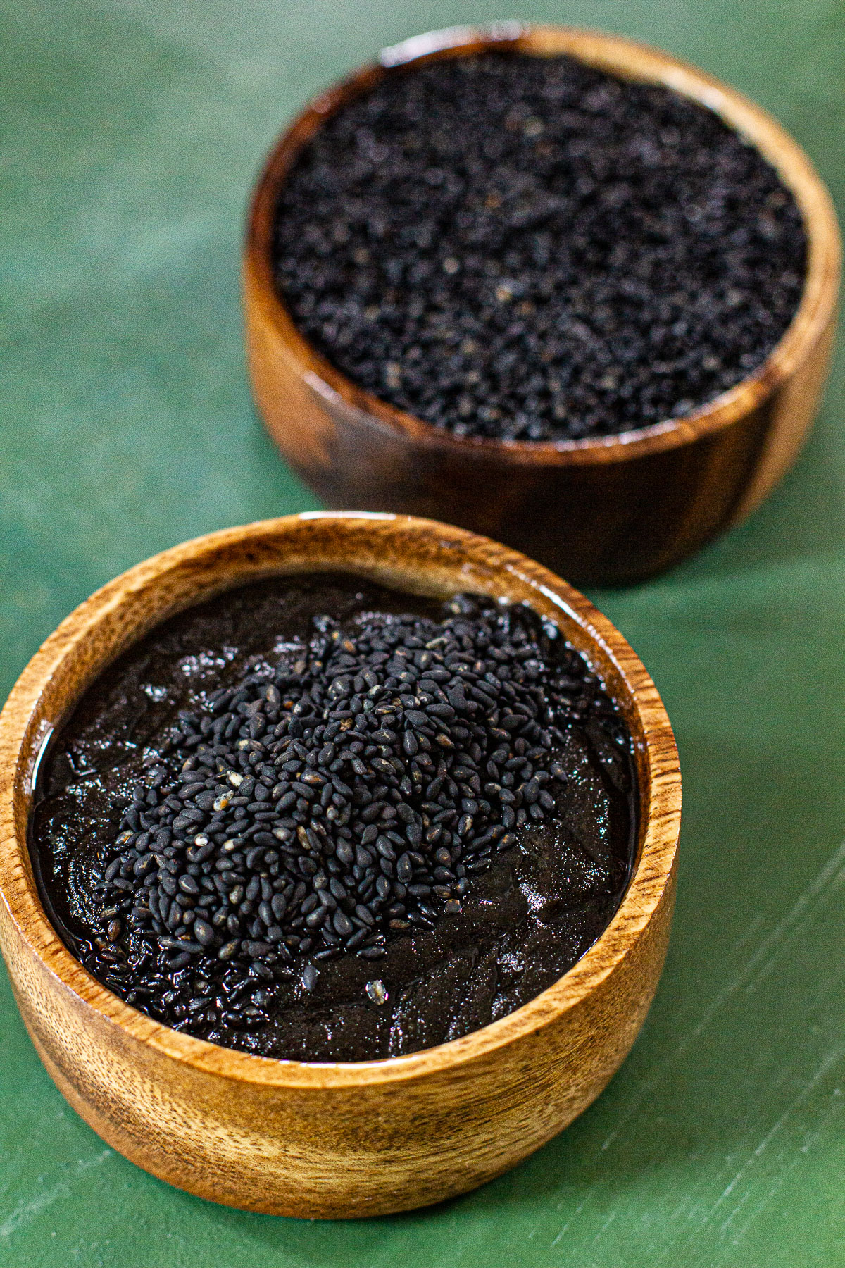 2 wooden bowls of Kalamay topped with black sesame seeds on a green backround.