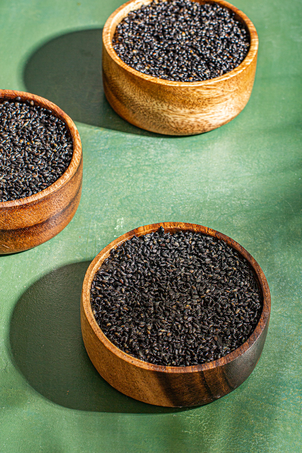 3 wooden bowls of Kalamay topped with black sesame seeds on a green backround.