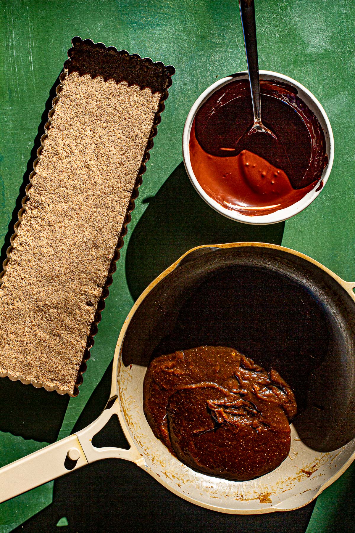 Polvoron pressed in a tart tin, melted tableya and matamis na bao in a skillet on a green backdrop.