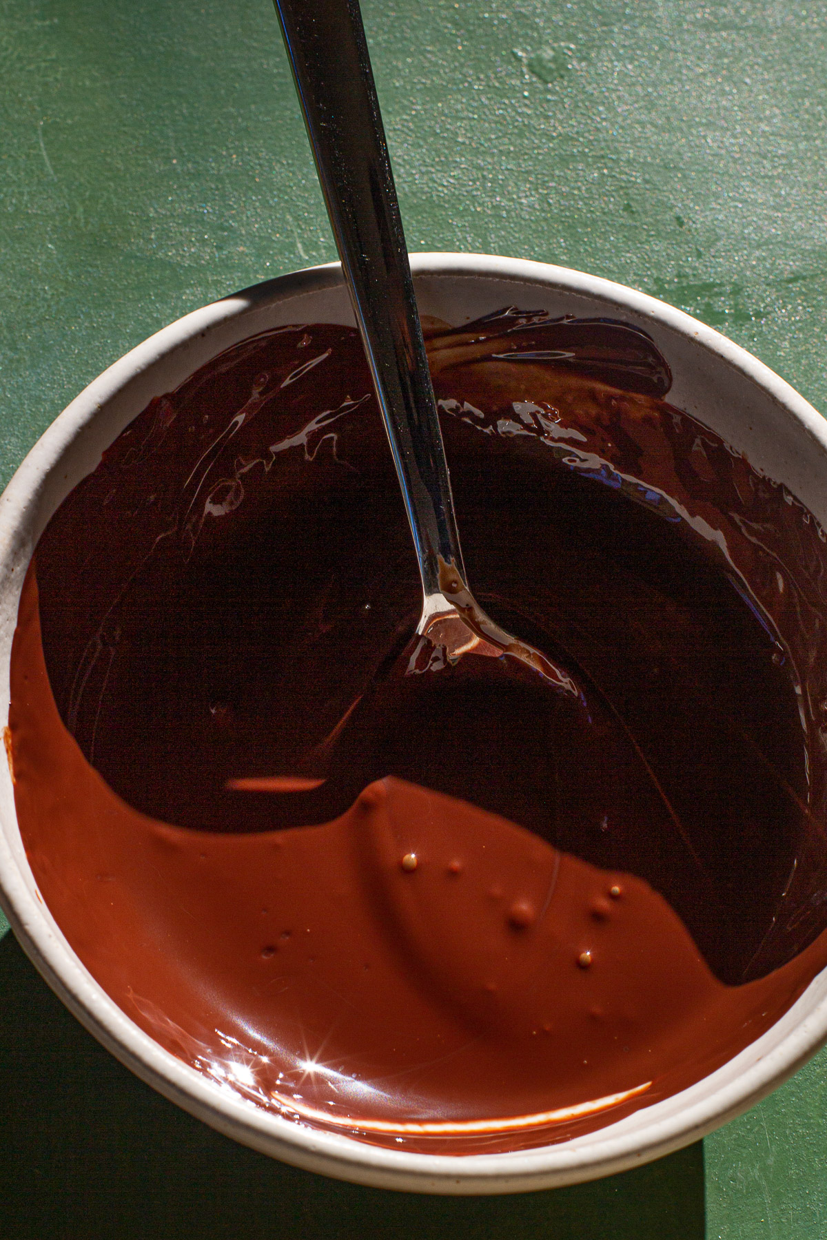 Melted tableya in a bowl with a spoon inside on a green backdrop.