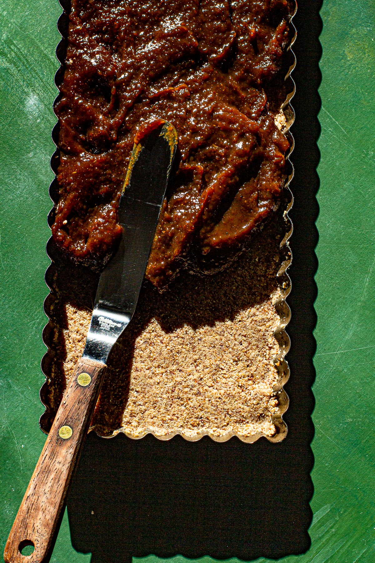 Matamis na Bao being spread on top of a polvoron base using an offset spatula in a tart tin. Using a green backdrop.