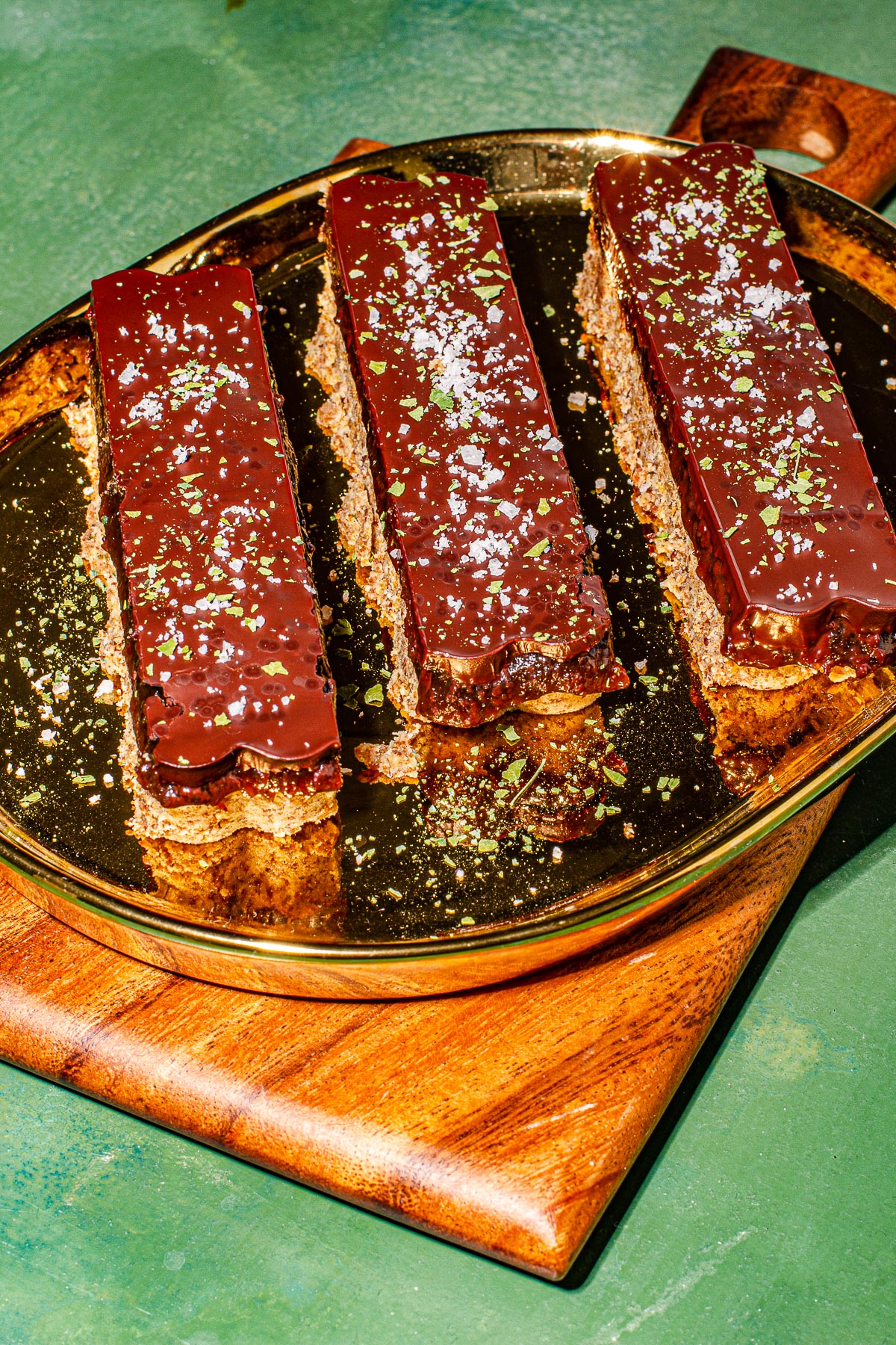3 bars of Millonariyo Bars (Filipino Style Millionaire Bars) on a gold plate on a small cutting board. All on a green background.