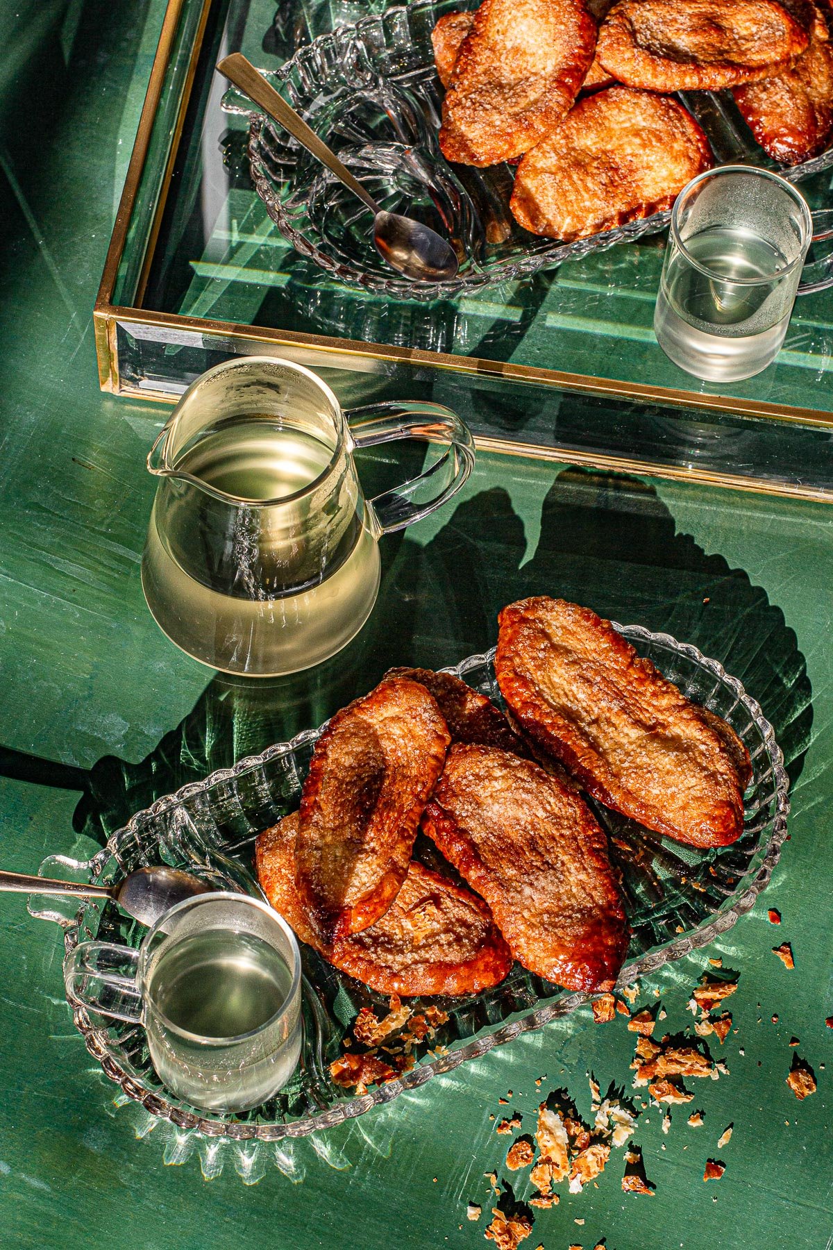 Otap on a glass plate with salabat in cups and pitcher. Gold and glass tray on green back drop.