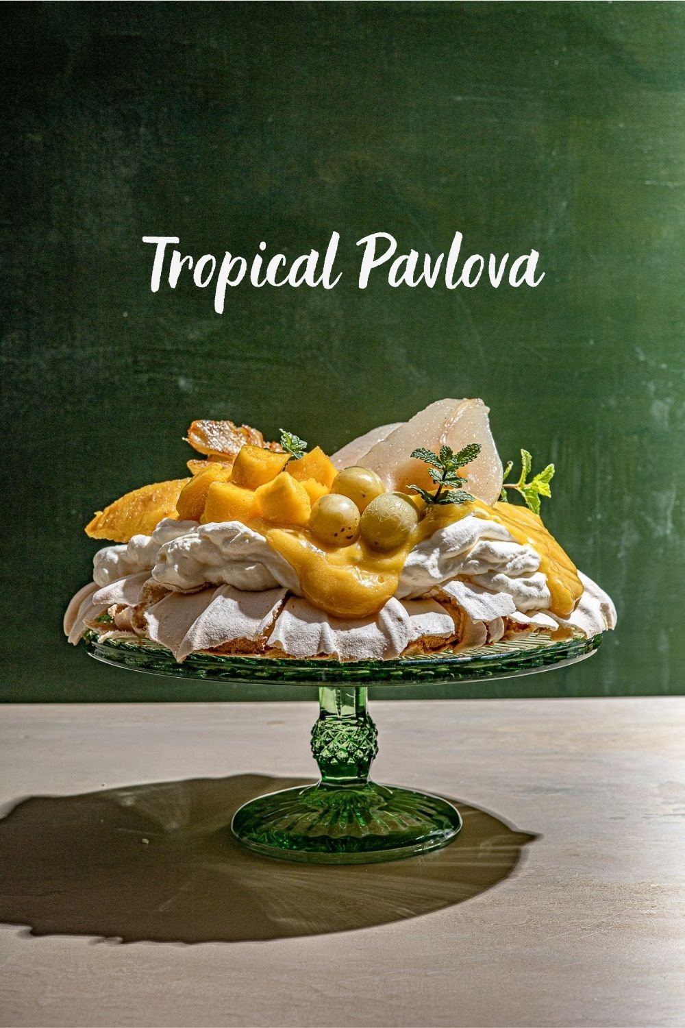 Tropical Pavlova on a green glass cake stand with a green backdrop.