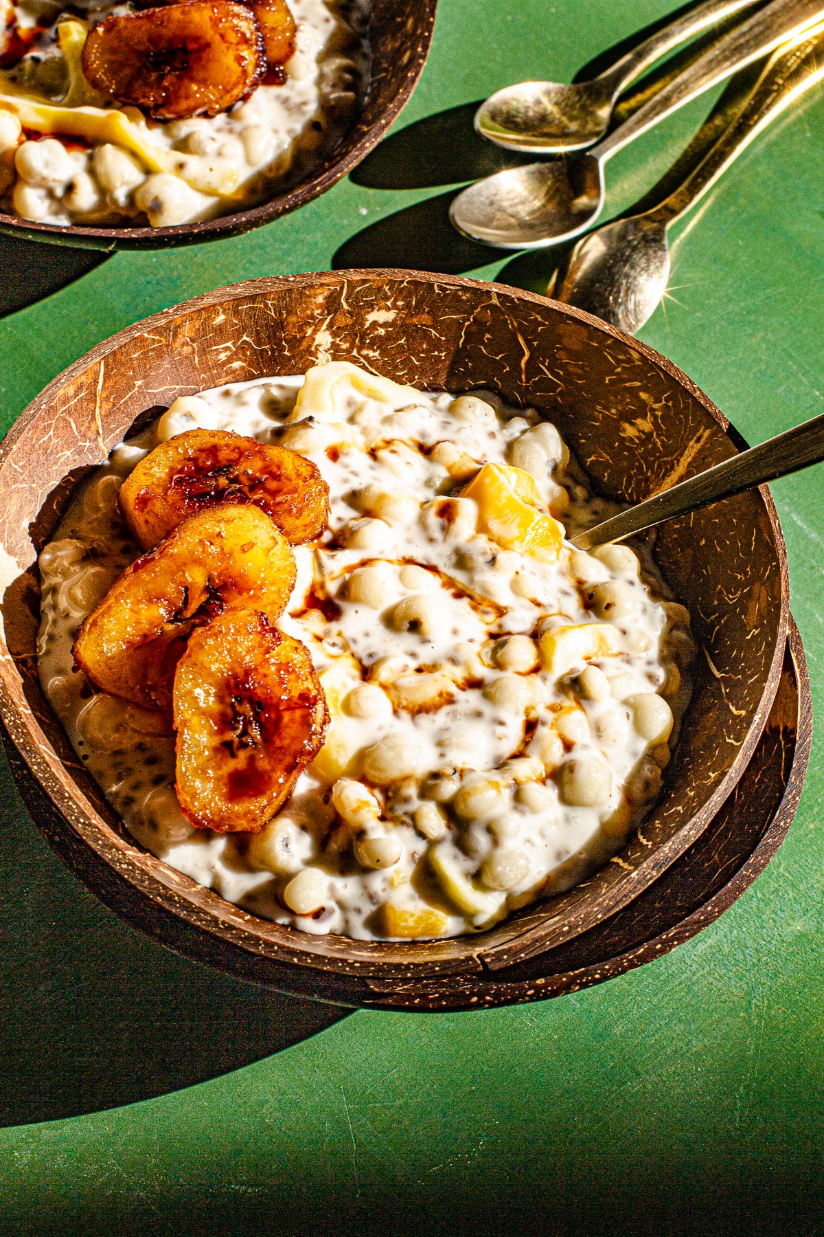 Two bowls of Ginataang Adlai with golden spoons on a green backdrop.