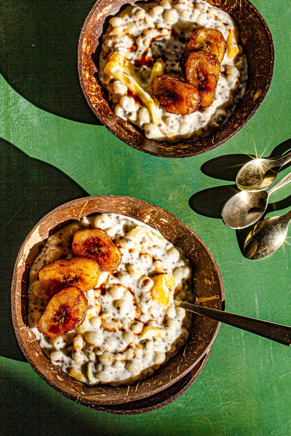 Two bowls of Ginataang Adlai with golden spoons on a green backdrop.