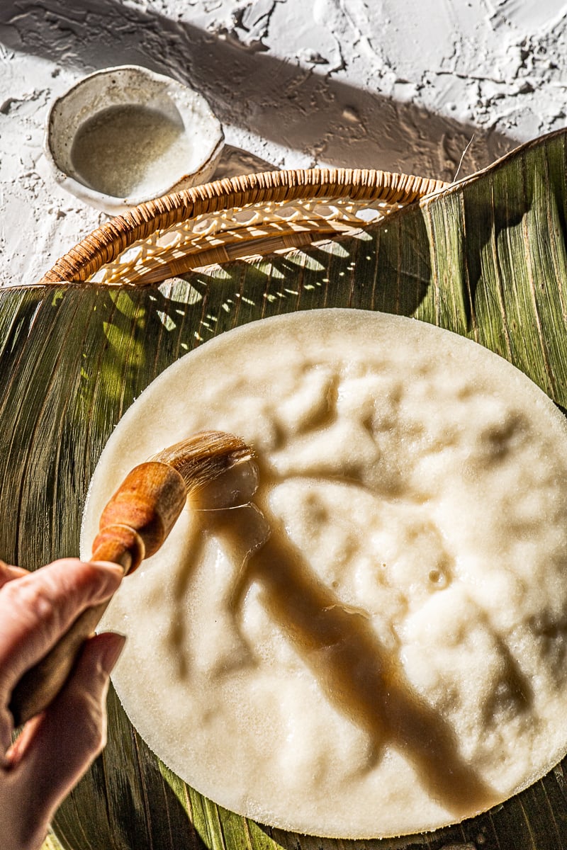 Puto brushed with melted butter with a pastry brush. On a banana leaf with melted butter in a bowl on the side.