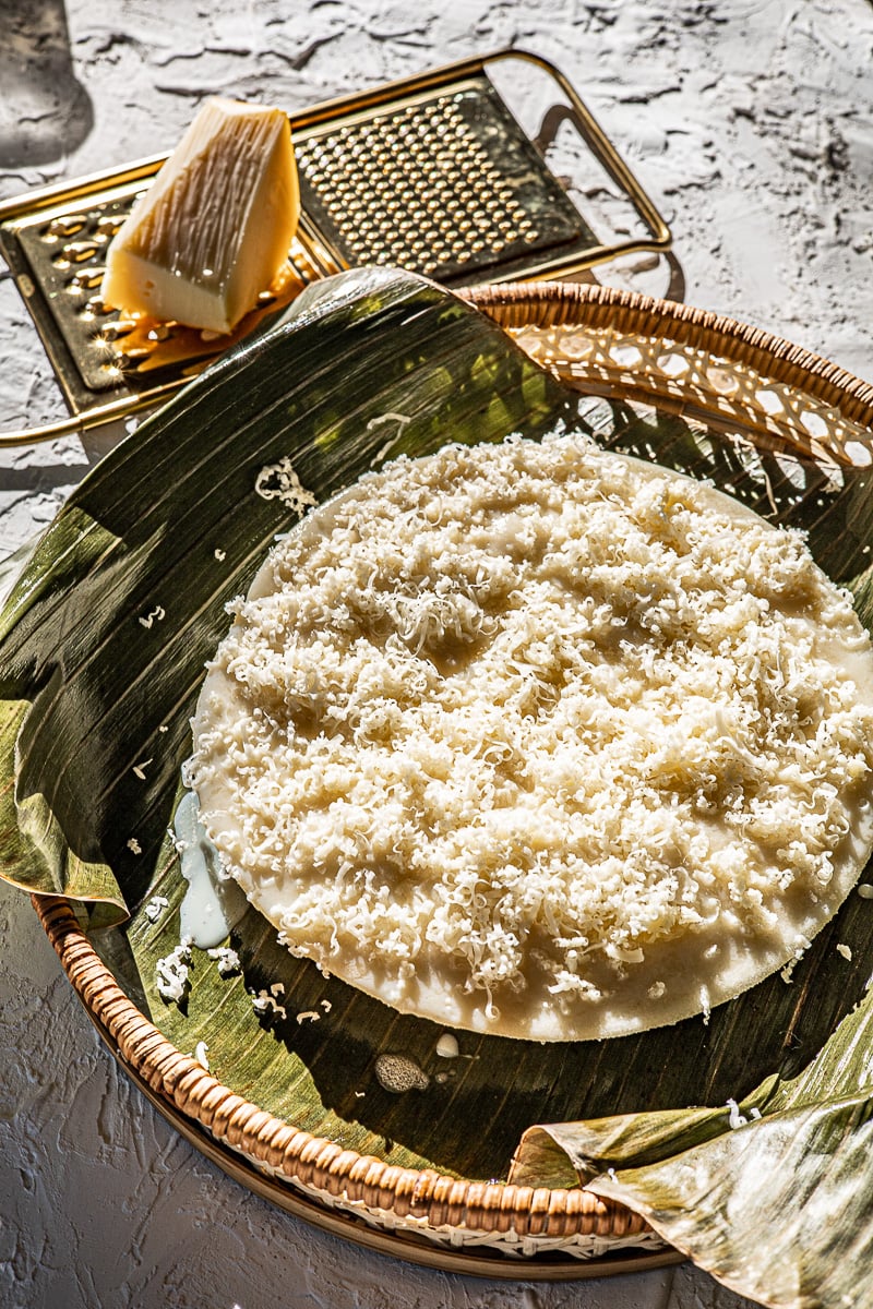 Cheese on a golden grater and puto with grated cheese on top on a banana leaf.