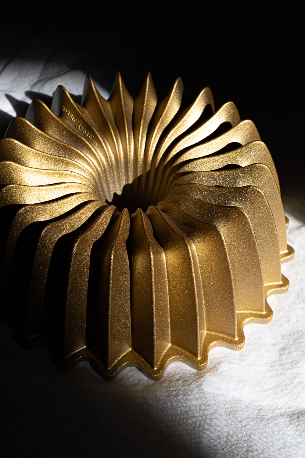 Gold bundt pan on a white table cloth with black shadows.