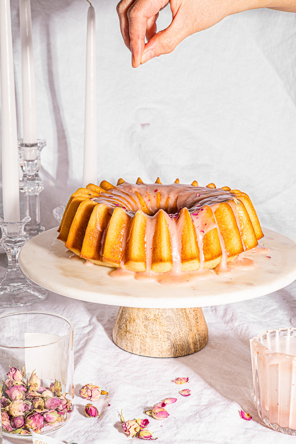 A hand adding rose petals to the Ispahan Cake on a marble cake stand.