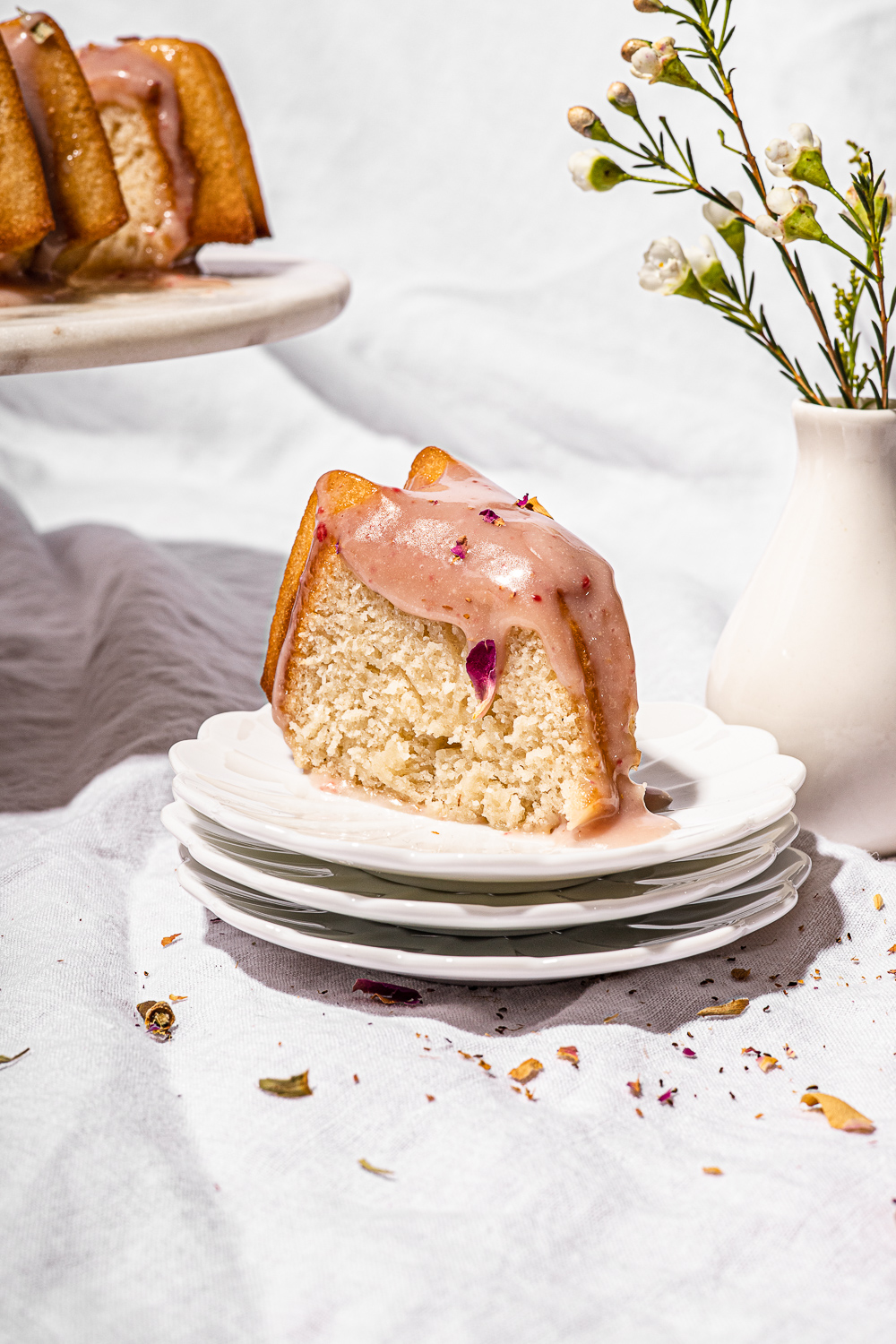 Slice of Ispahan Cake on 3 white small plates with a bud vase in the background.