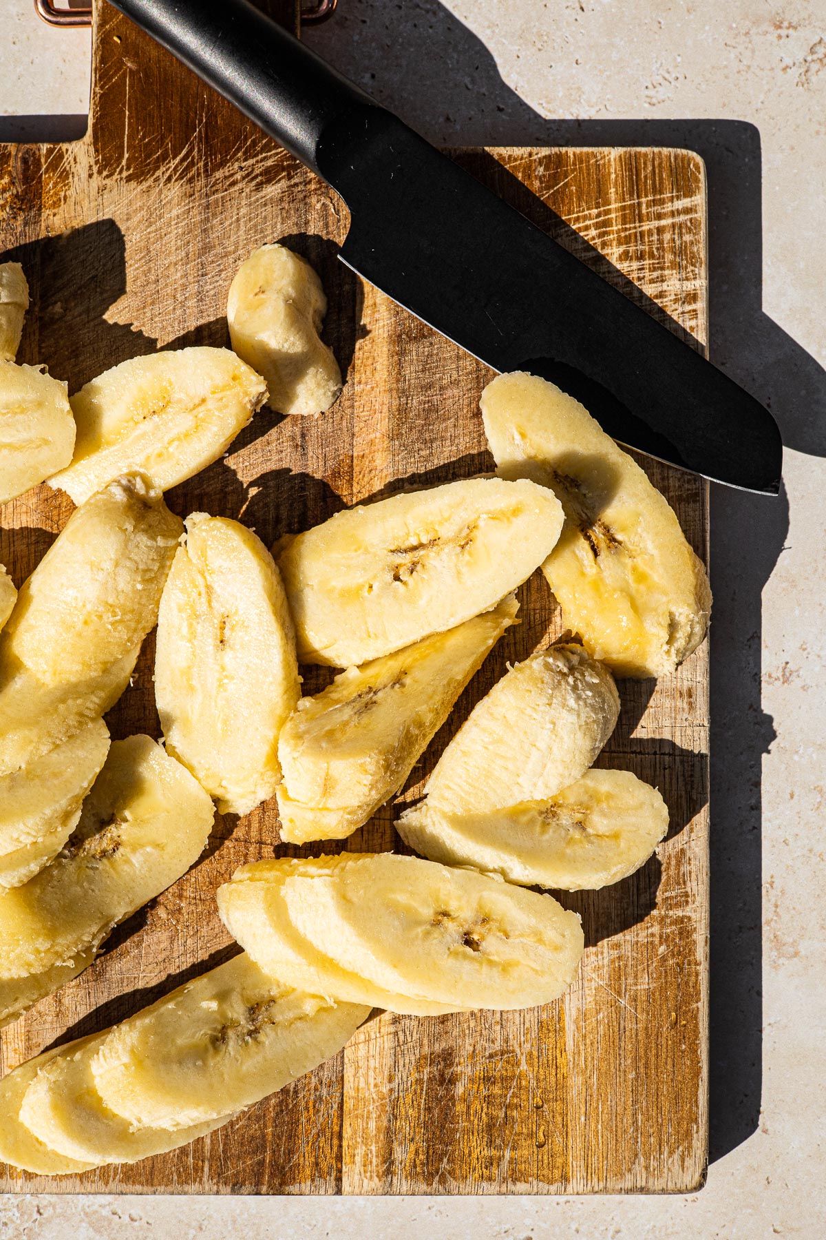 Saba Bananas cut diagonally on a cutting board with a black knife on the upper right side.