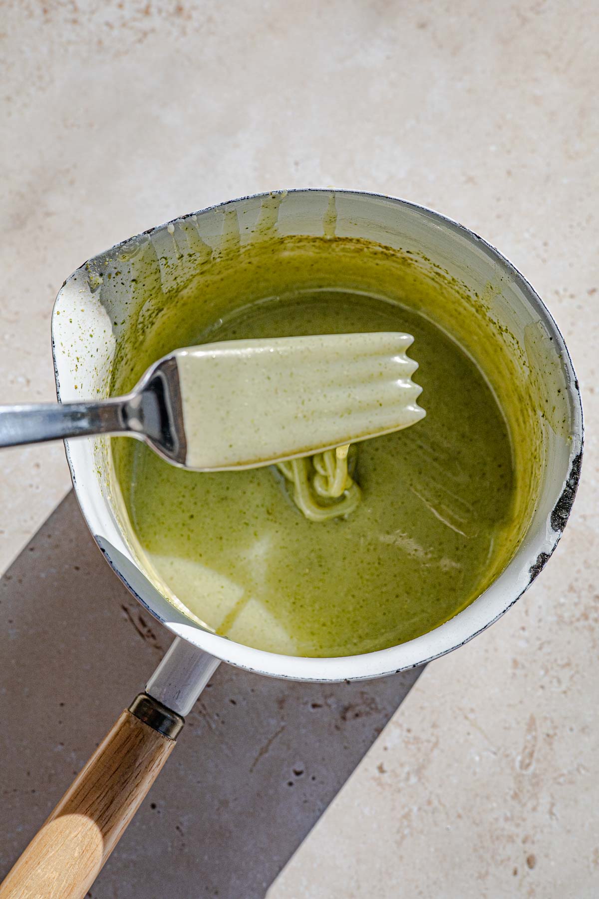 Pandan ganache drizzle in a sauce pan with a fork drizzling.