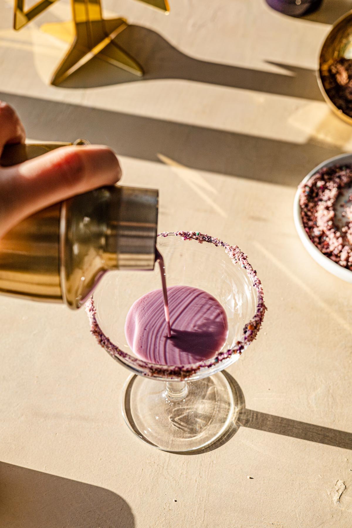 Cocktail shaker pouring Ube Eggnog into a coup.
