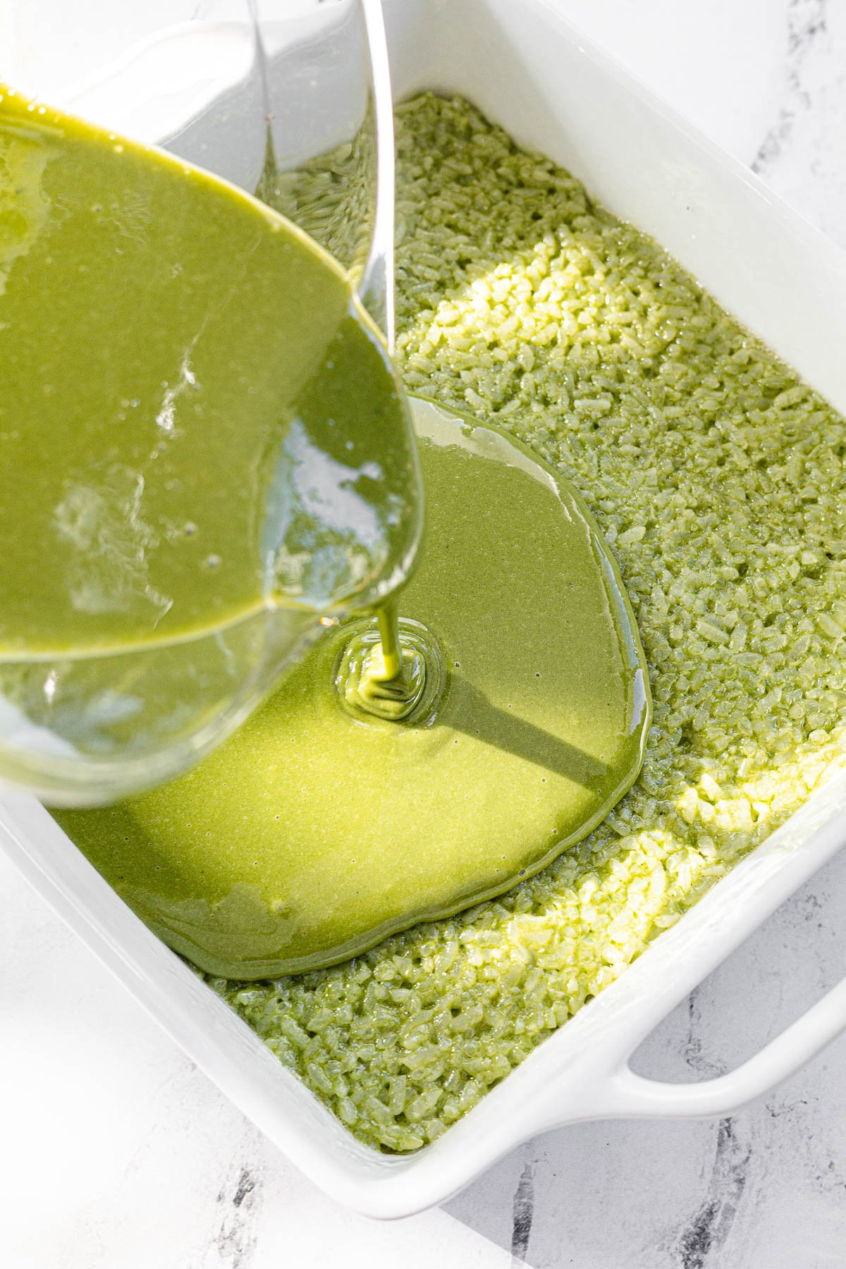Matcha custard in glass bowl being poured into cooked Biko.