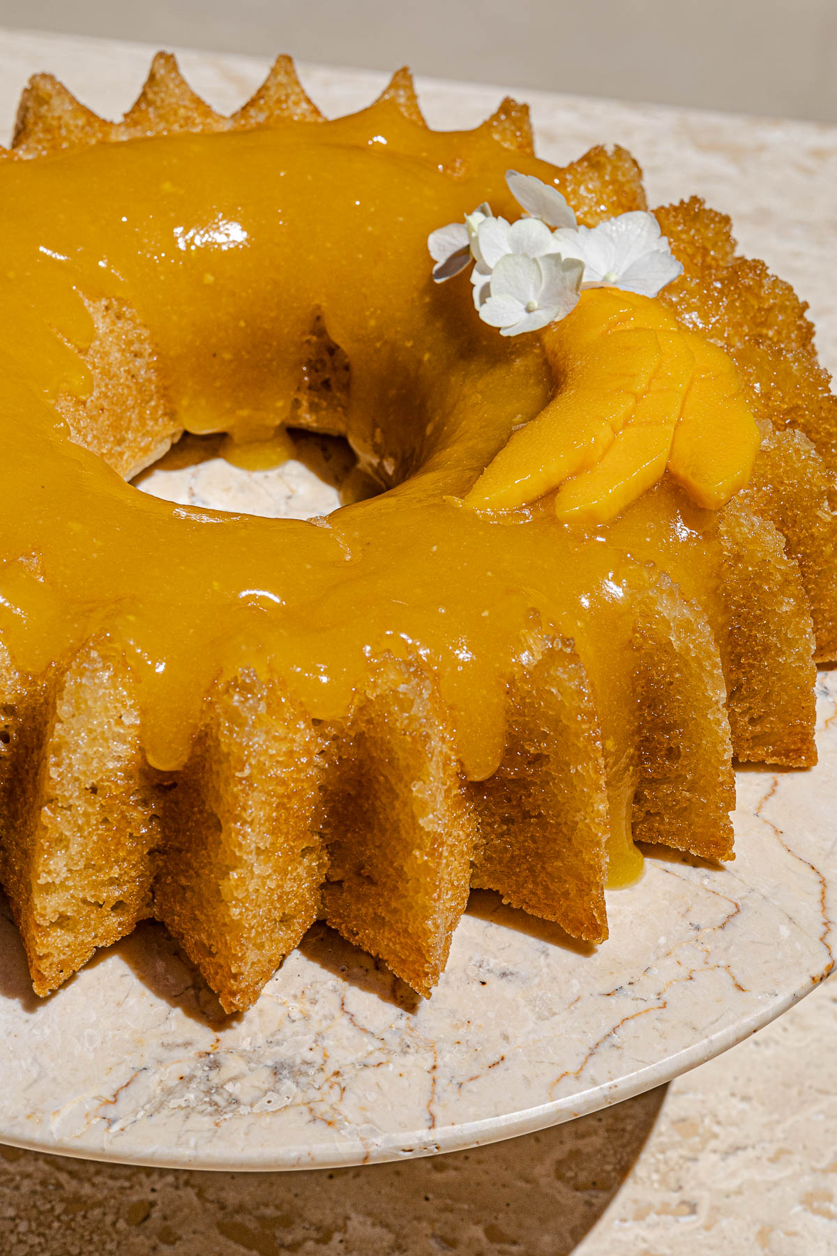 Vegan Mango Cake with Mango Glaze and fresh sliced mango with white flowers.