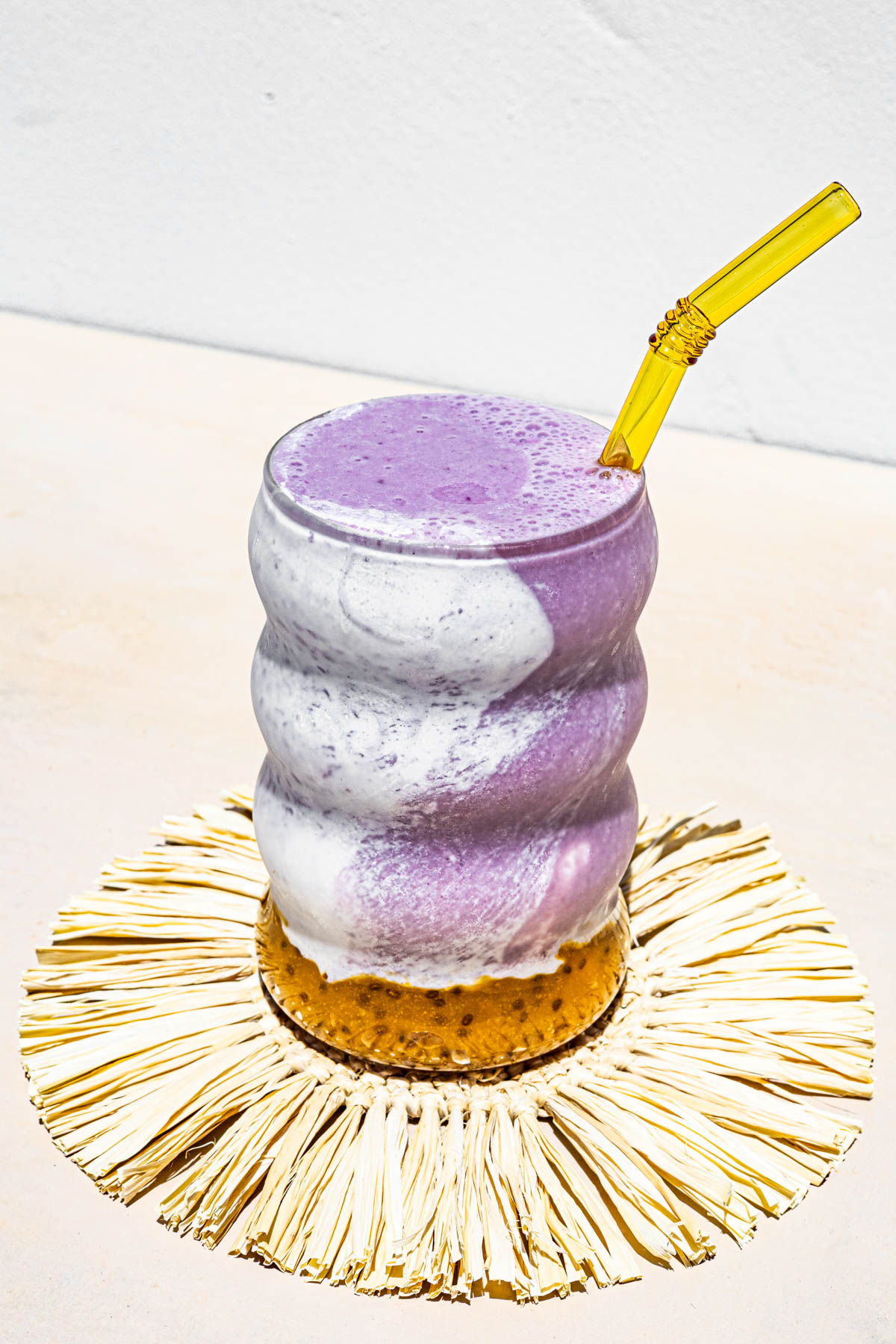Sapin Sapin Smoothie in a glass with a yellow glass straw on top of a grass coaster.