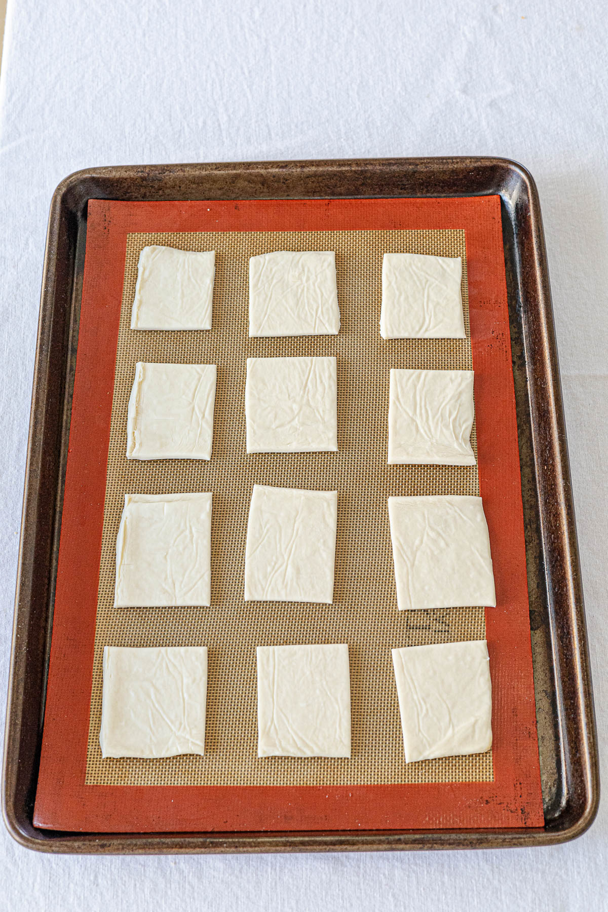 Half a sheet of puff pastry cut into 12 squares on a baking sheet.