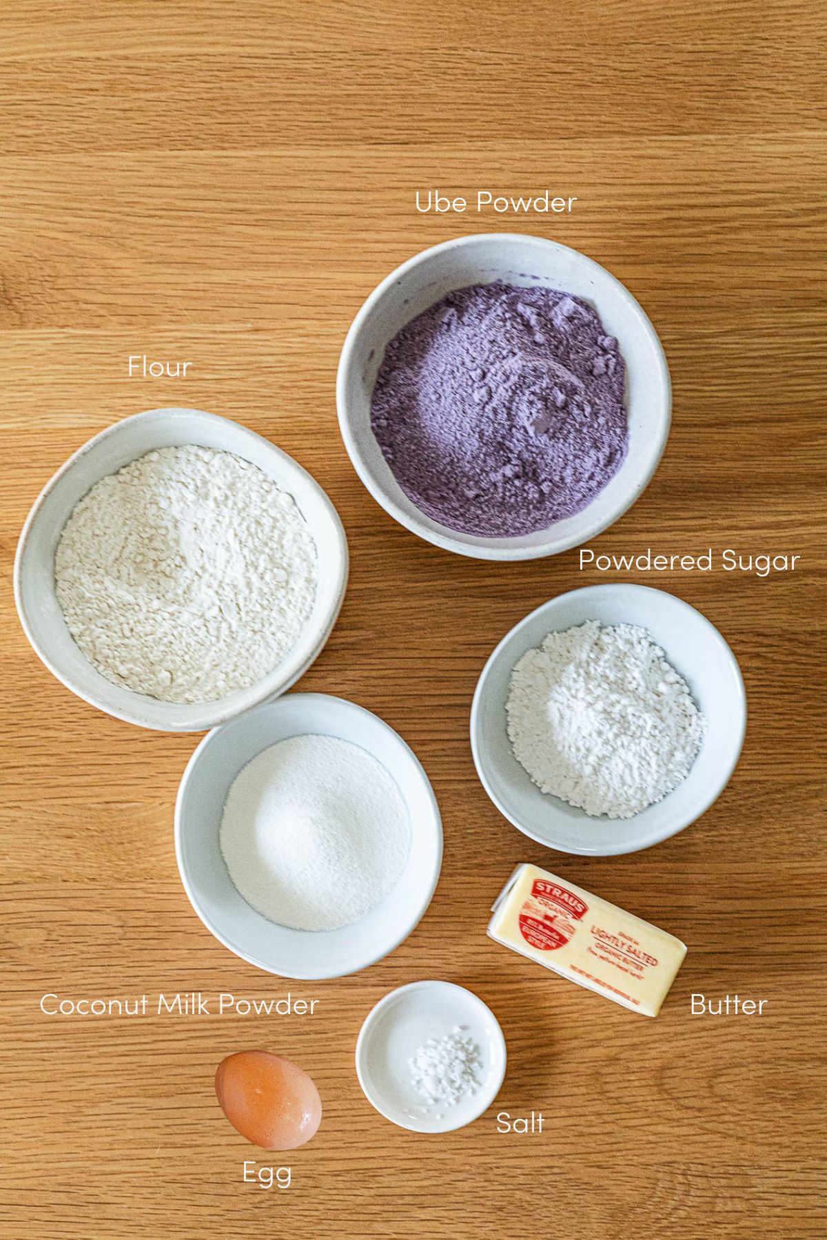 Ingredients: Ube powder in a bowl, flour in a bowl, powdered sugar in a bowl, coconut milk powder in a bowl, a stick of butter, salt on a plate and one egg.