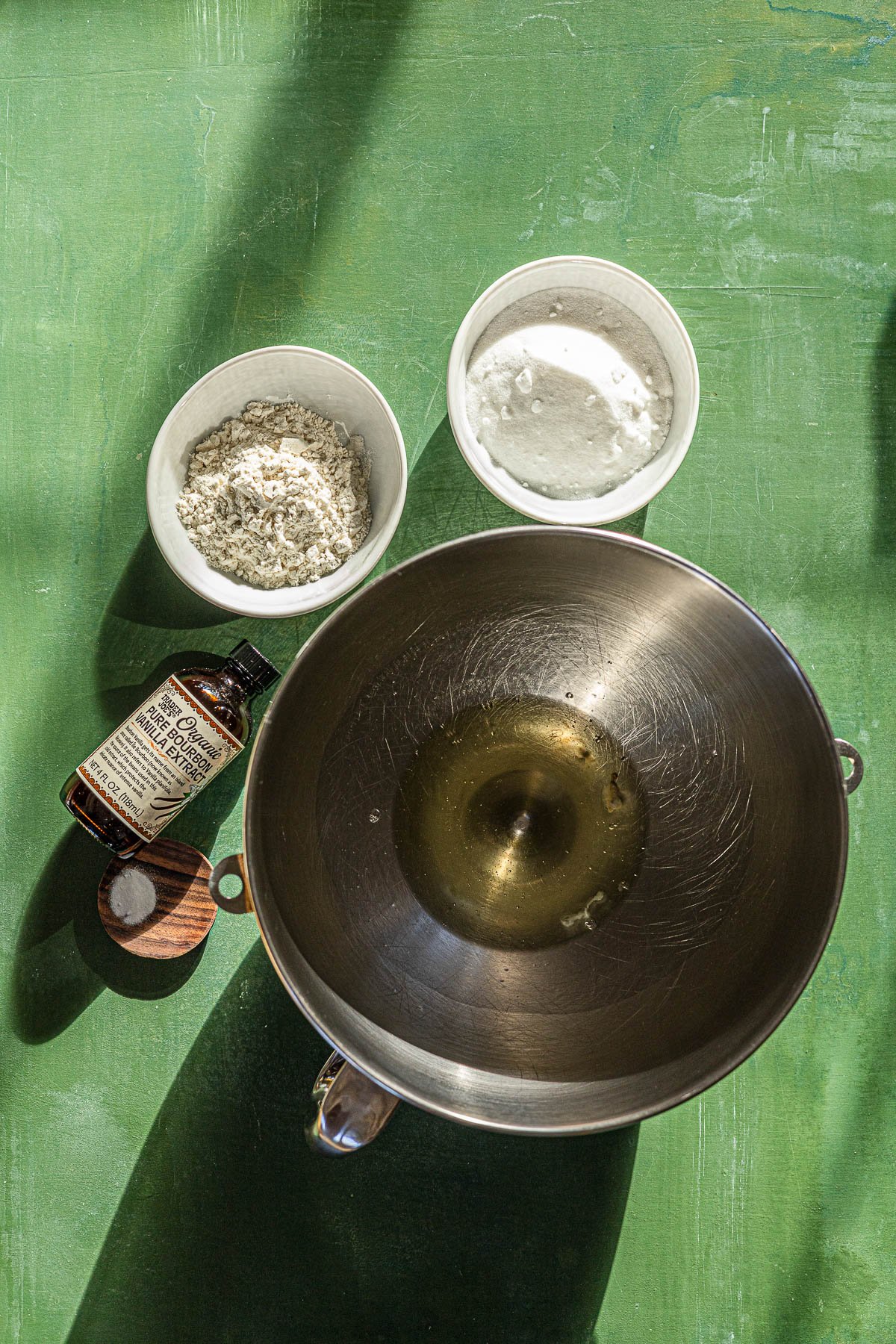 Bowl of egg whites, bowl of sugar, bowl of flour, bottle of vanilla extract and small plate of baking soda.