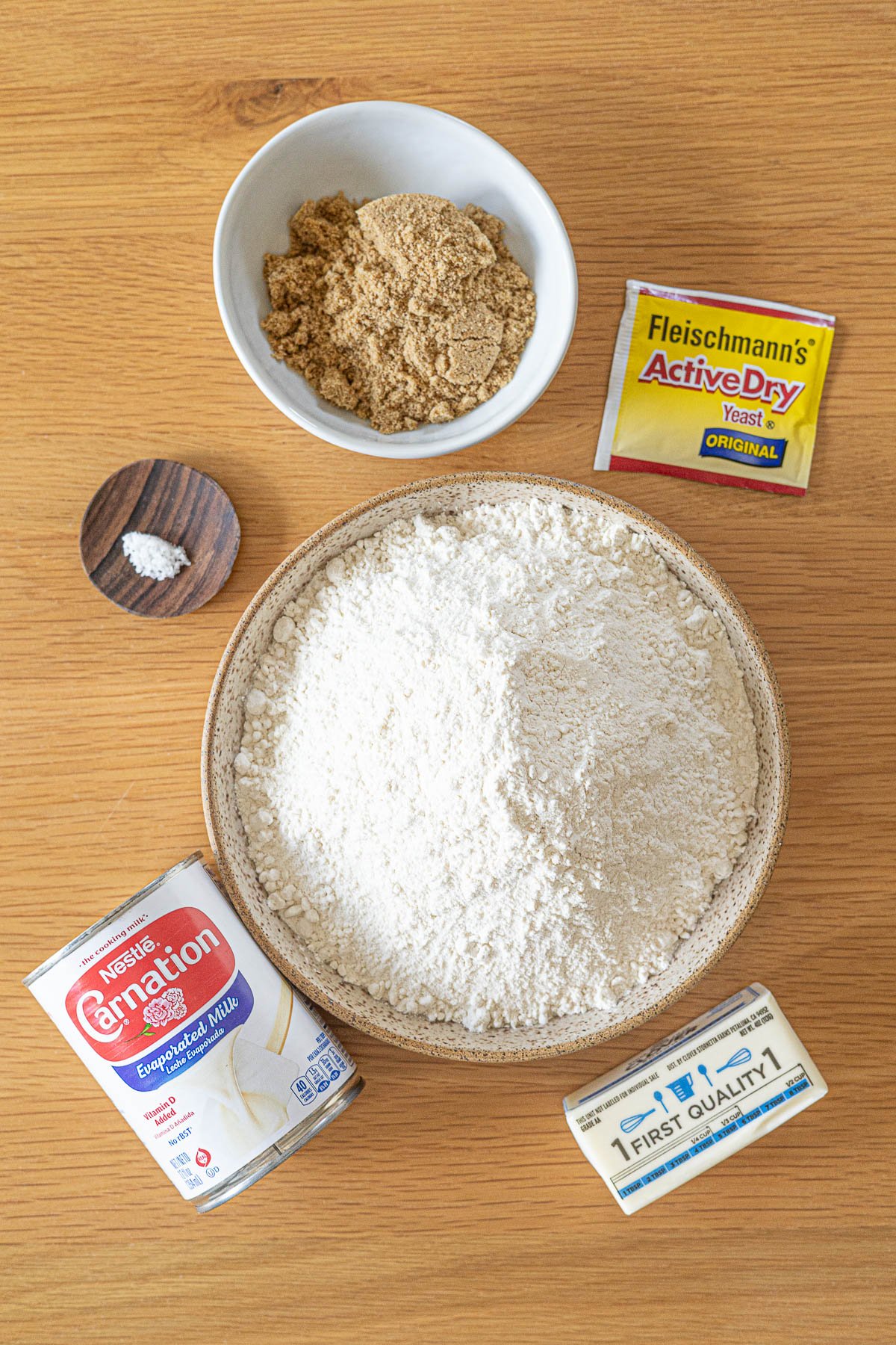 Bowl of muscovado sugar, bowl of bread flour, salt, can of evaporated milk, packet of yeast and bar of butter.